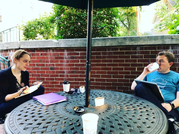 Two writers discussing their work at an outdoor table.