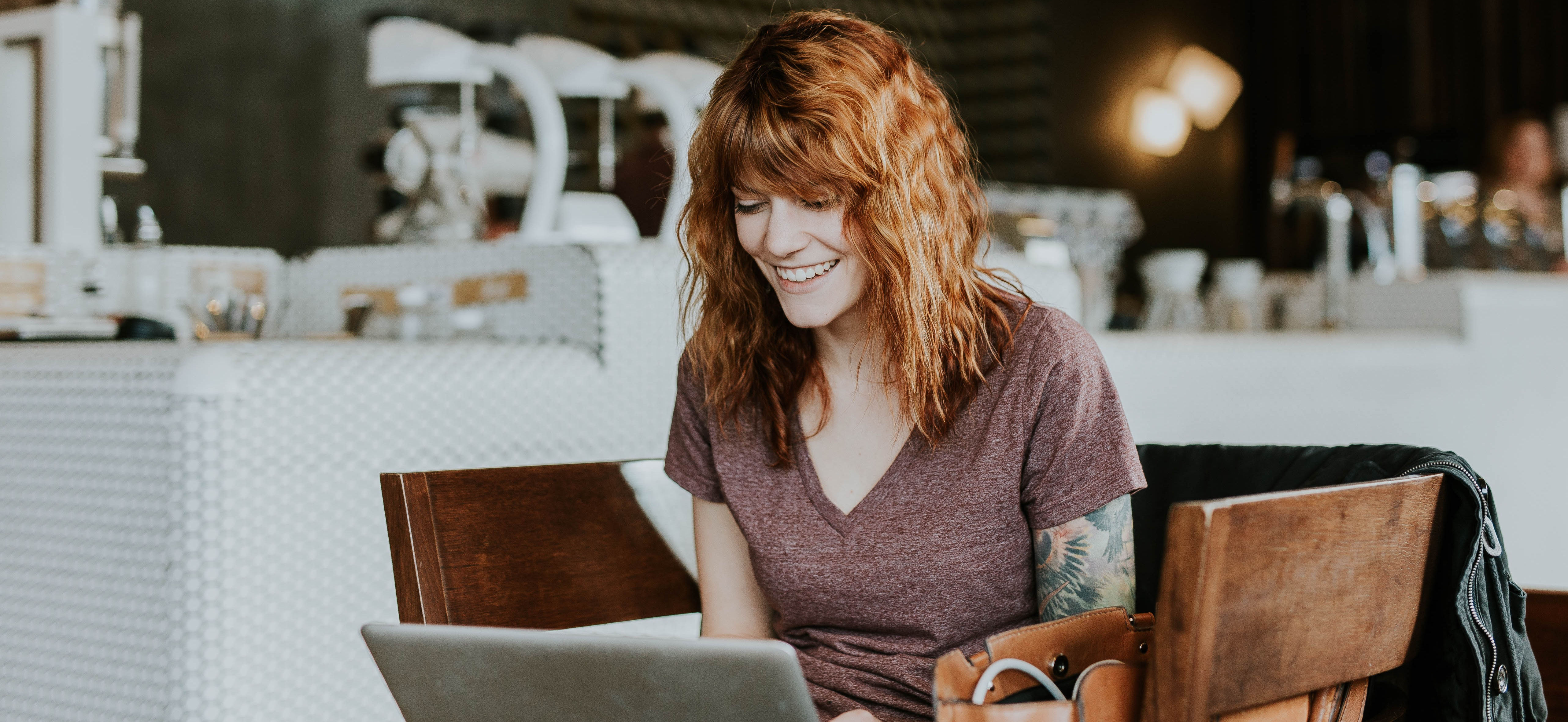Woman sitting in a cafe with a laptop, smiling and looking delighted