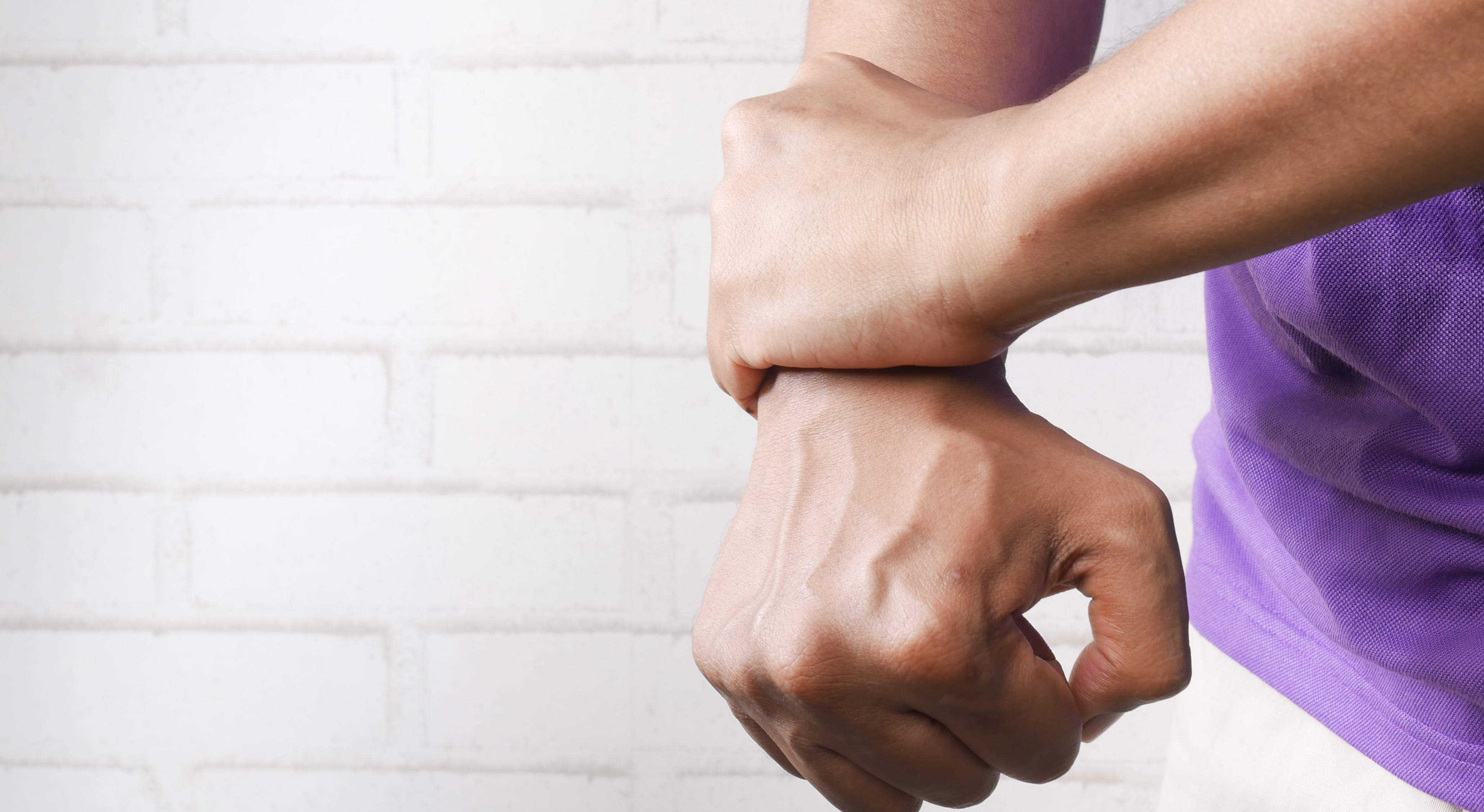a person with a clenched fist using their other hand to grip the wrist, as if in pain